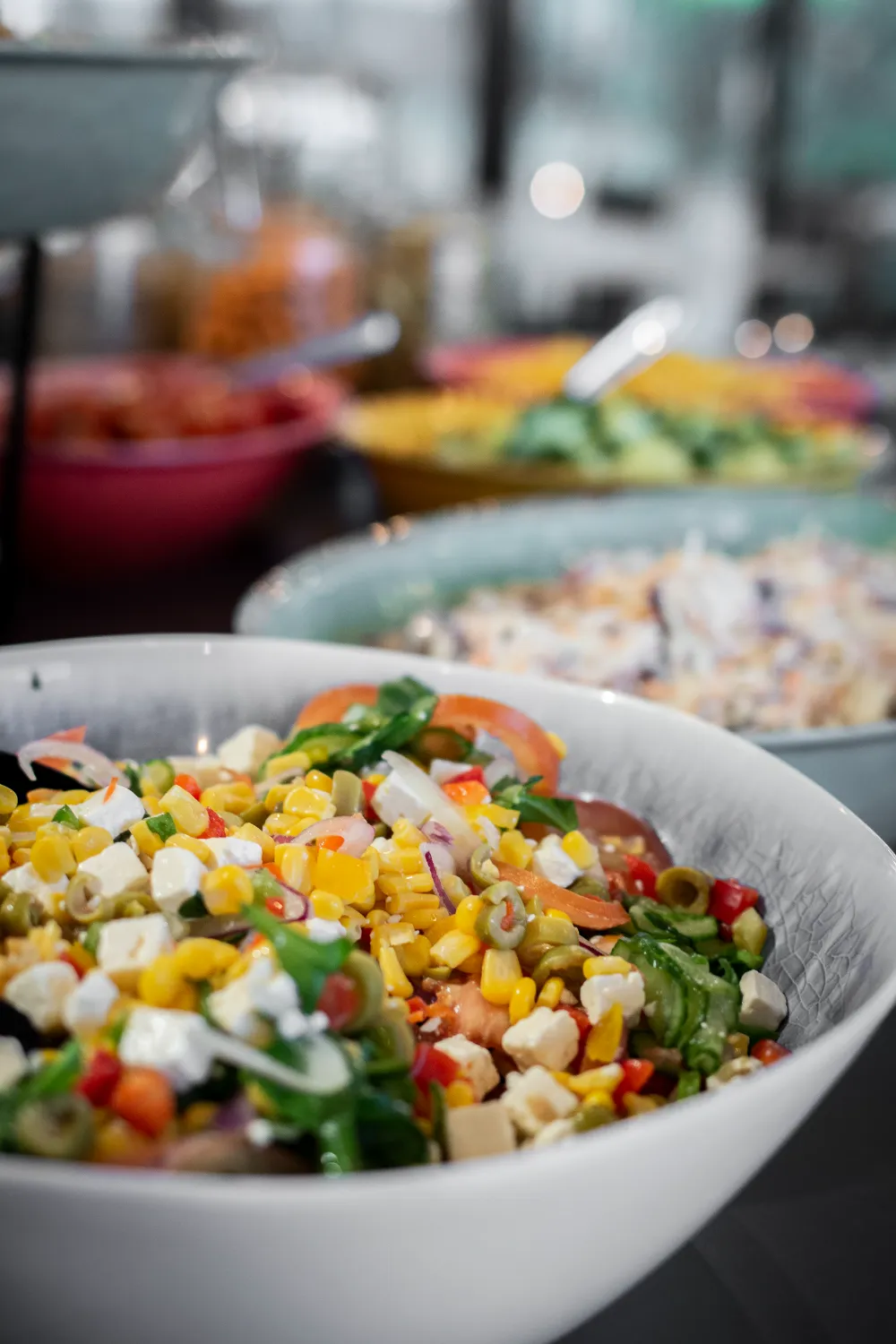 Frokostordning Viby - Farverig salat buffet med friske grøntsager, majs, fetaost og urter serveret i hvide porcelænsskåle, med flere forskellige salater i baggrunden